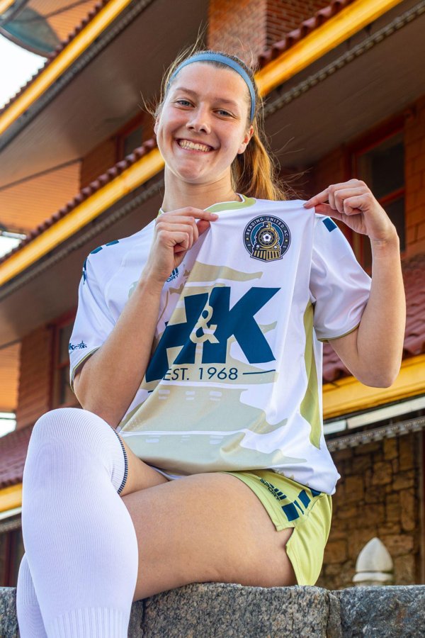 RUAC player holding up a home match shirt, showing the front-of-shirt logo placement